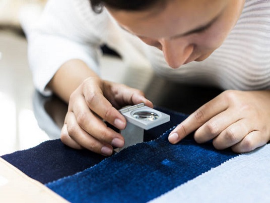 Young woman examining fabric quality with magnifier